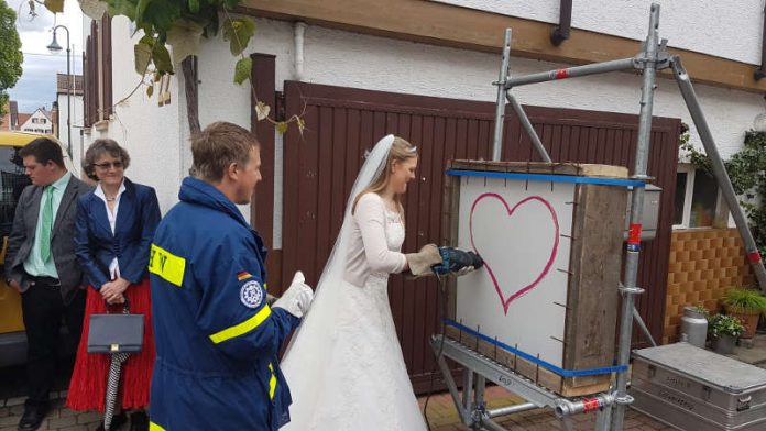 Die Braut schneidet das Herz mit der Säbelsäge aus, nachdem ihr Bräutigam (in THW-Jacke) zuvor das Eisengitter entfernte (Foto: THW)